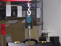 Hanging scales PCE-HS 150 weighing a briefcase to be shipped by a carrier company.